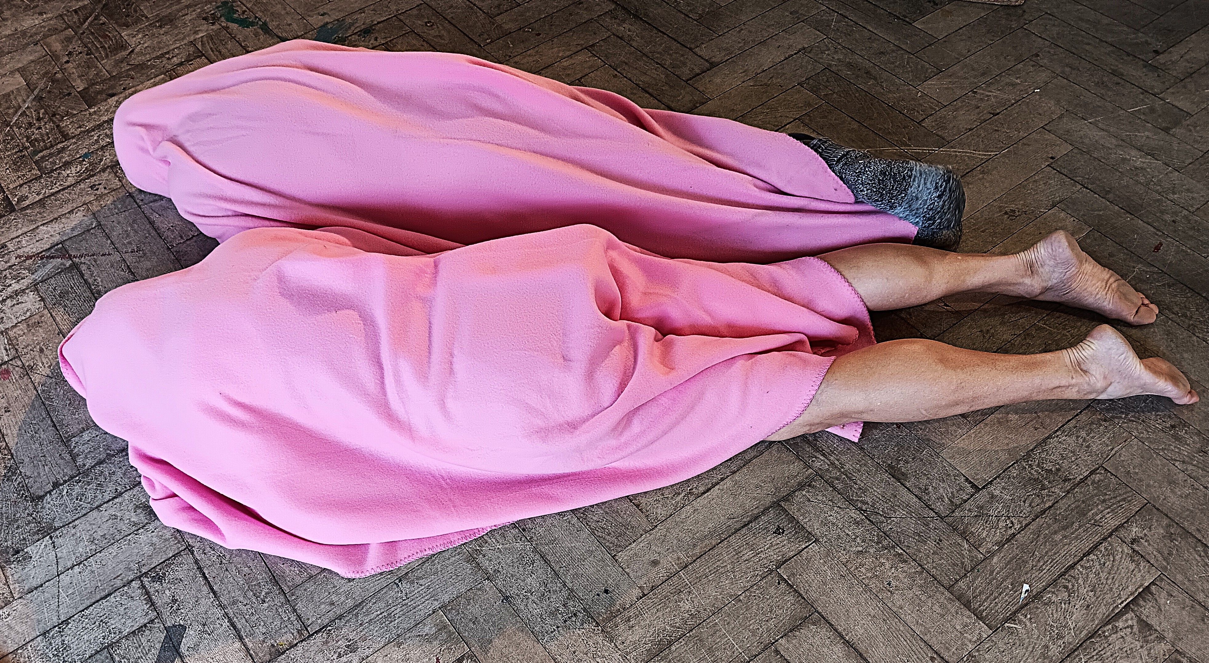 Zwei Personen unter rosa Fleecedecken liegen auf dem Boden. Man sieht nur die nackten Beine und Füße.