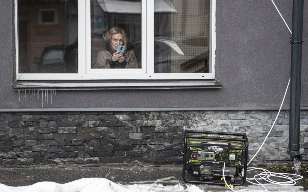 Person fotografiert mit Handy aus einem Haus auf die Straße. Vor dem Haus steht ein Generator