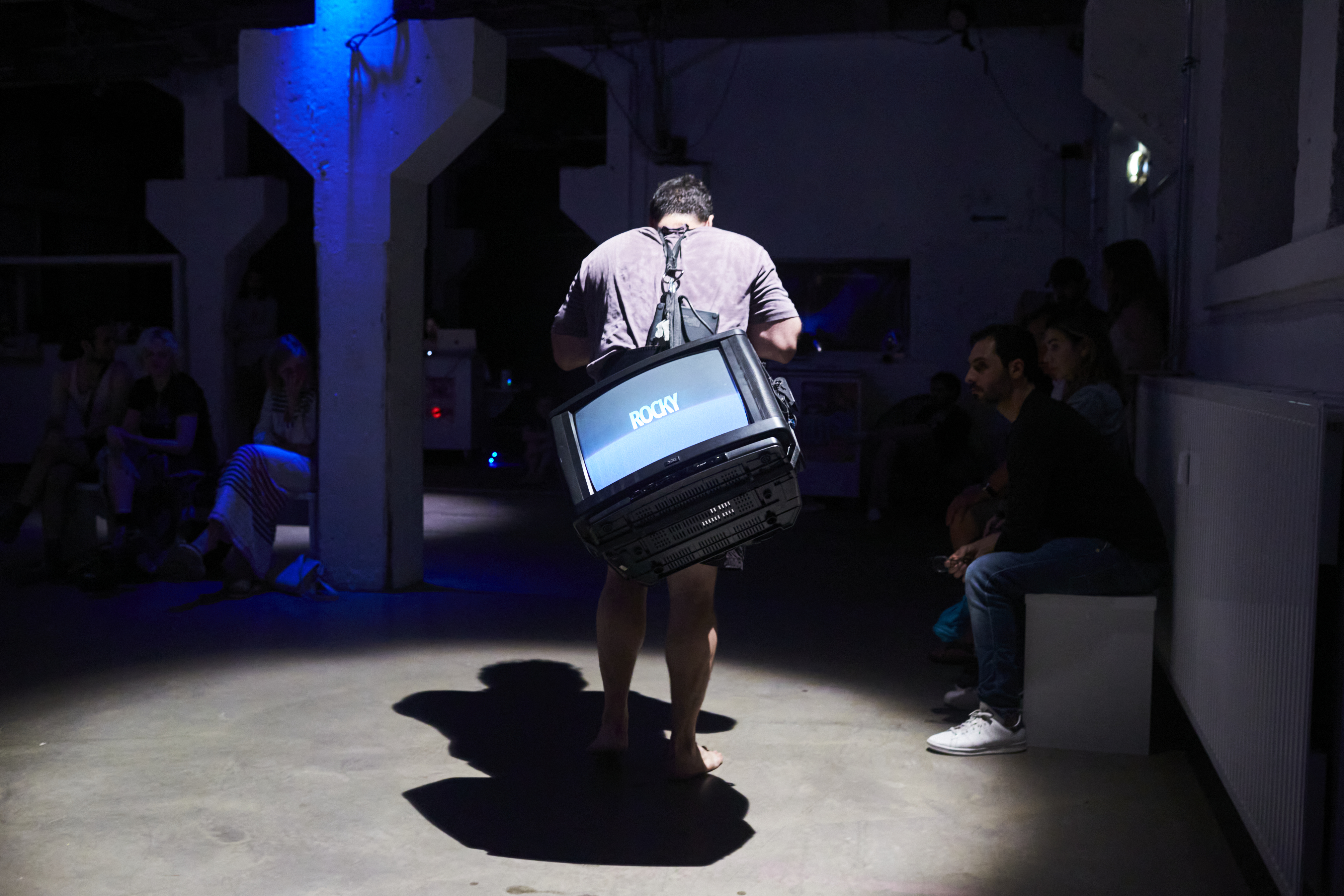 Person läuft mit einem Fernseher auf dem Rücken durch einen dunklen Raum