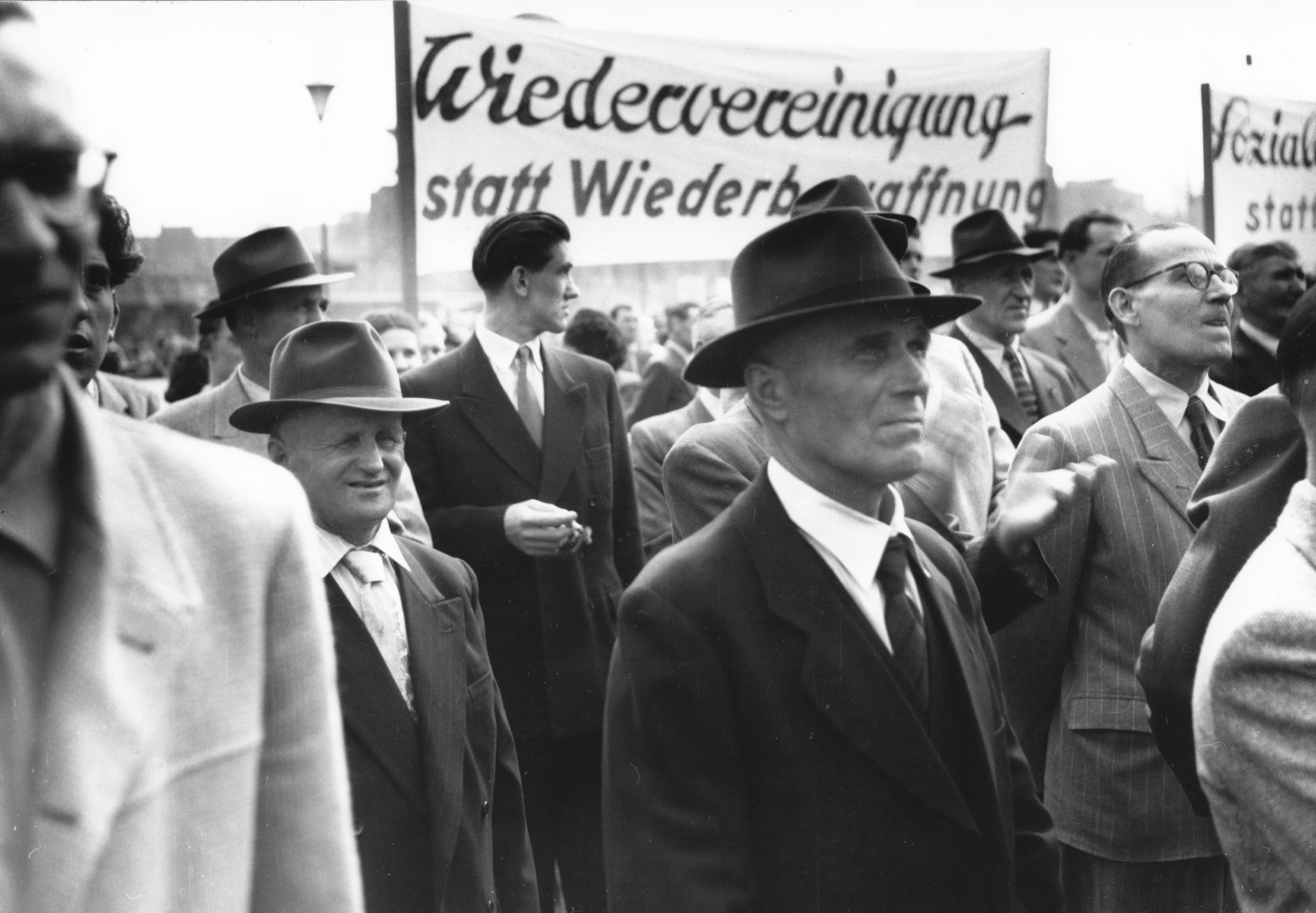 Historisches Bild von Menschen bei einer Demonstration mit einem Schild, das Wiedervereinigung statt Wiederbewaffnung fordert